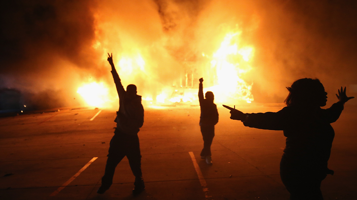 demonstrators cheer as fire rages behind them in Ferguson, Missouri