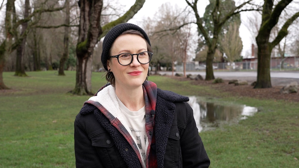 Tara Faul sits in a park while wearing a black coat and black beanie