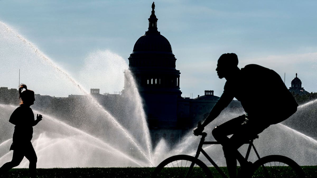 The Capitol is seen as water sprinklers soak the National Mall on a hot summer morning