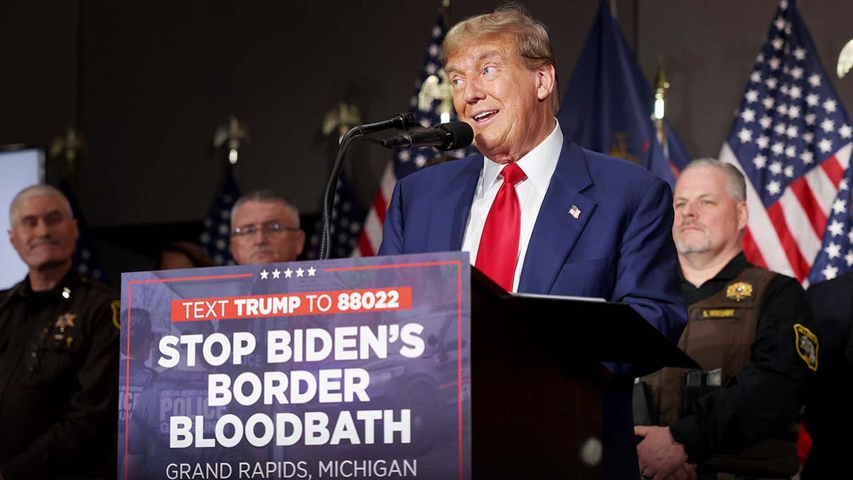 Trump at lectern with "Stop Biden's Border Bloodbath" sign on it