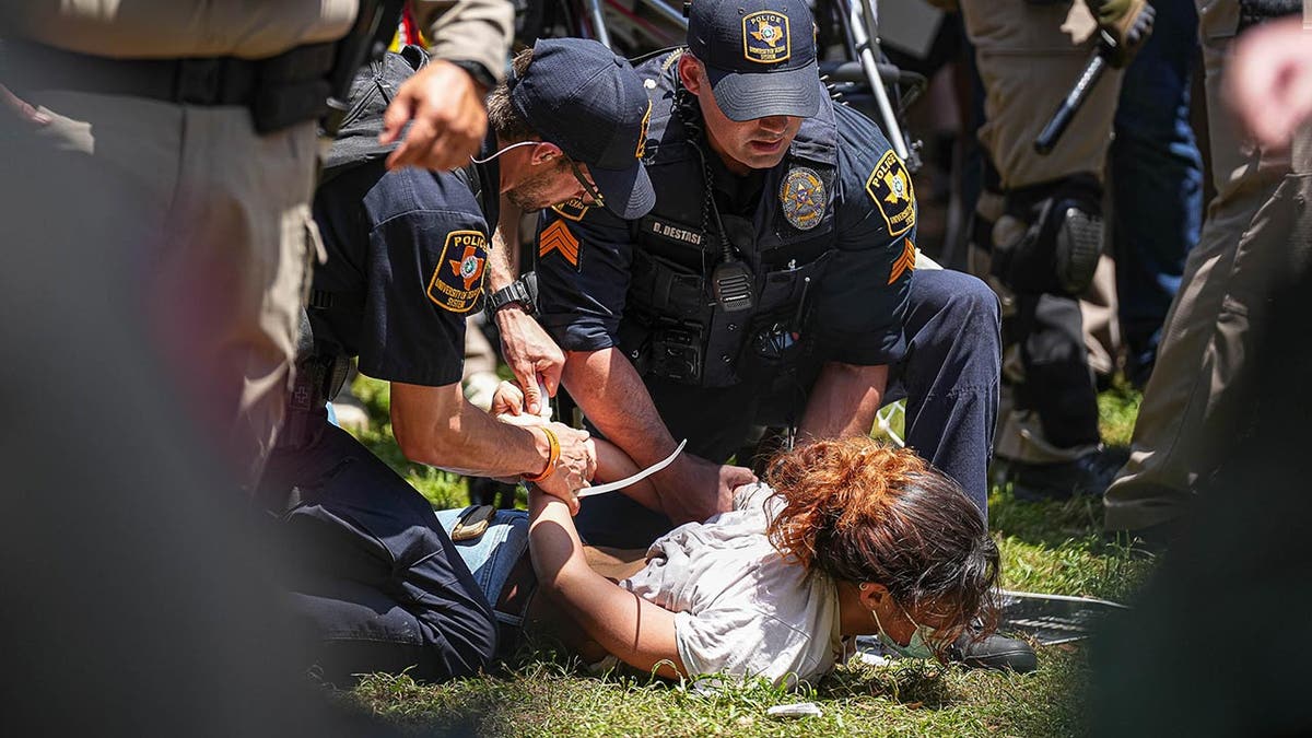 Police zip tie a protester who is face-down on the ground