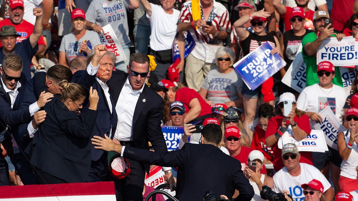 Donald Trump being shielded by Secret Service, raising fist in air