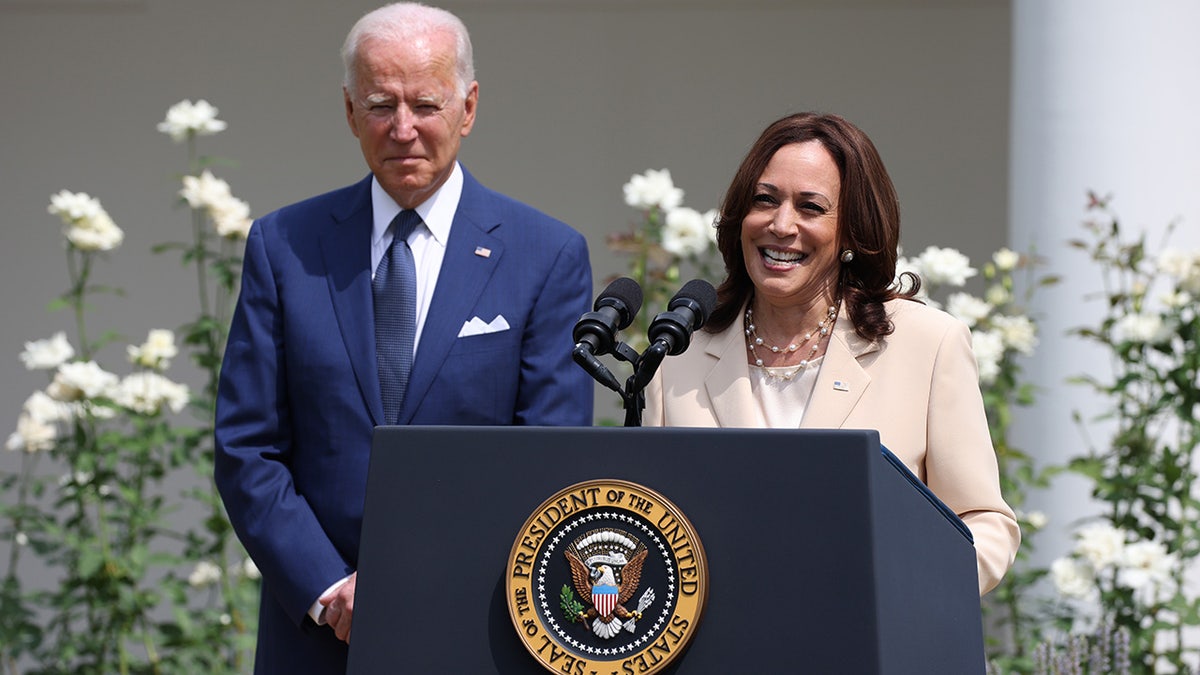 President Biden looking on behind VP Kamala Harris at lectern