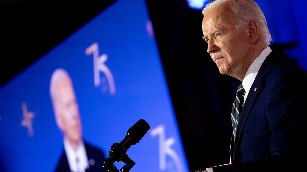 Joe Biden speaking, with big screen image of him off in background