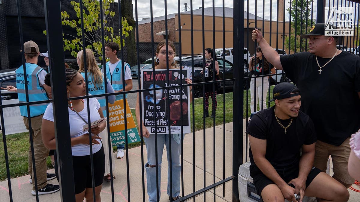 Protesters behind a fence hold up signs