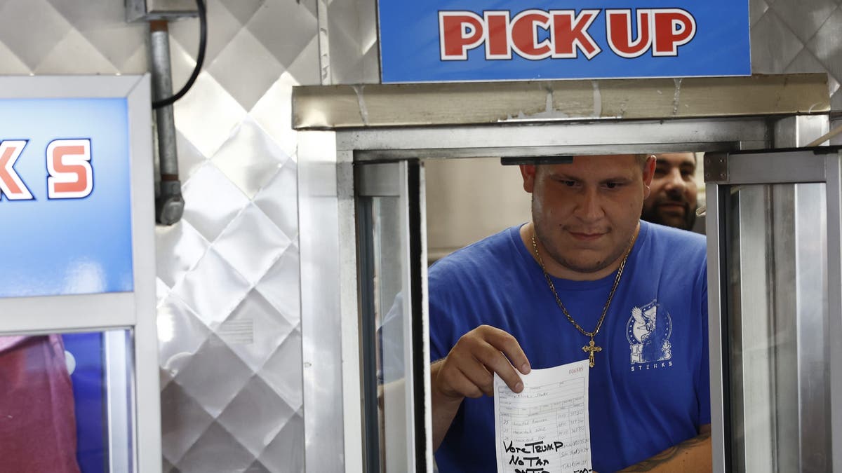 restaurant worker holds up a receipt with a note that reads "Vote Trump No Tax on Tip," signed by former President Trump