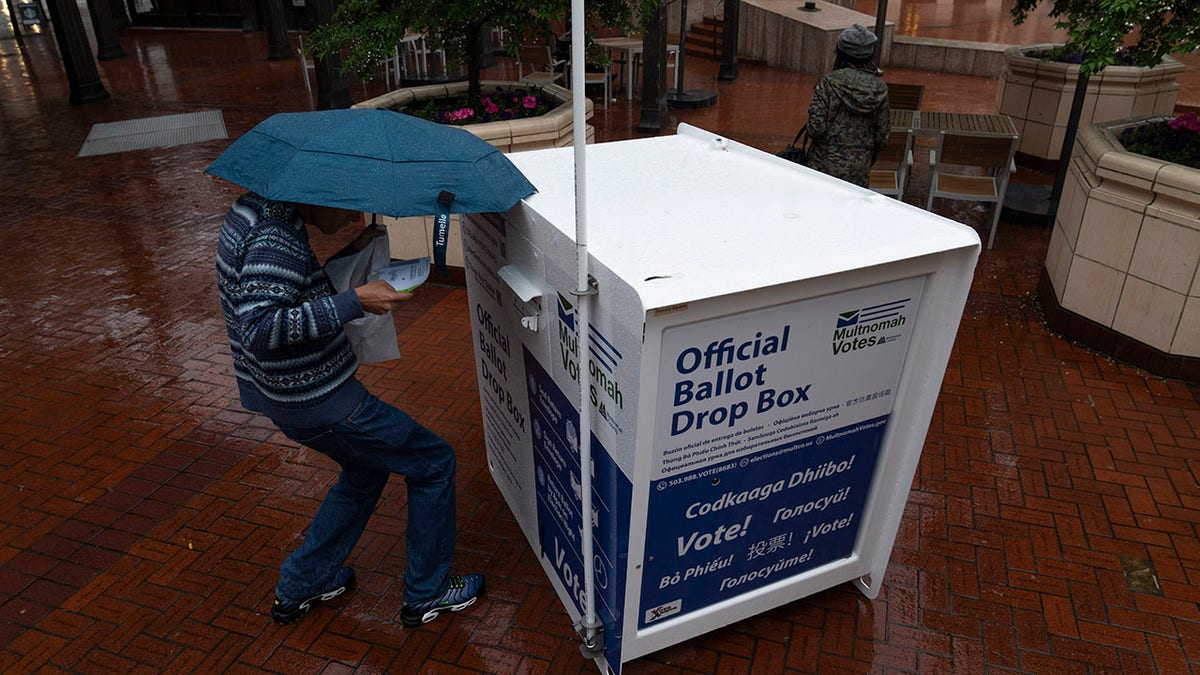 person voting in the rain by dropping ballot in outdoor box