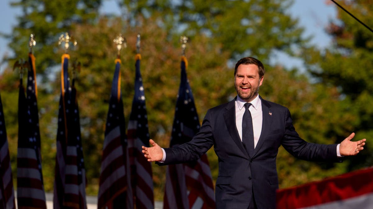 JD Vance with arms extended, flags behind him