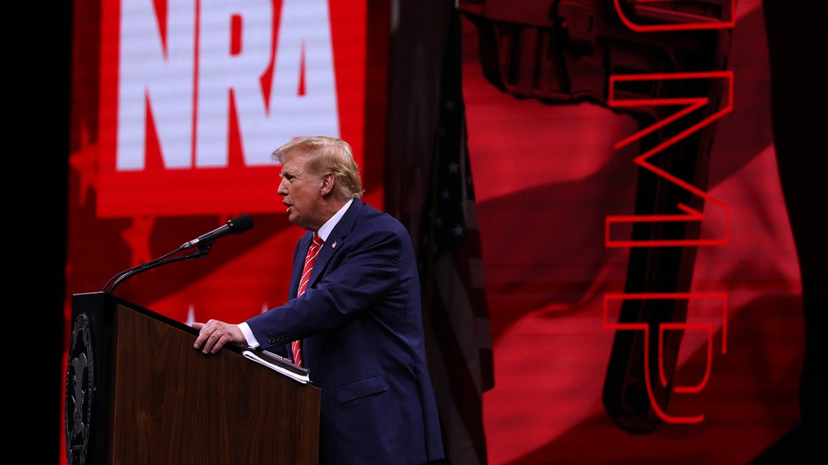 Donald Trump at NRA event podium, seen in wide profile shot