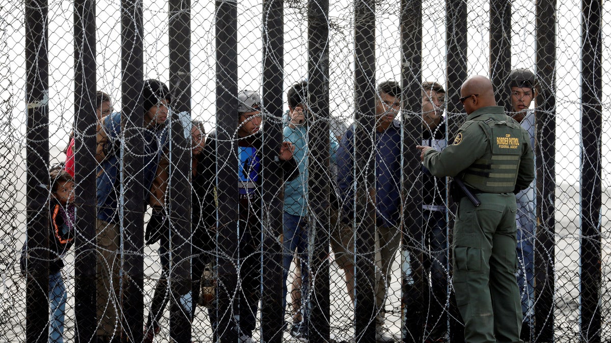 Customs and Border Protection border patrol agent talks to people on the Mexican side of the border wall