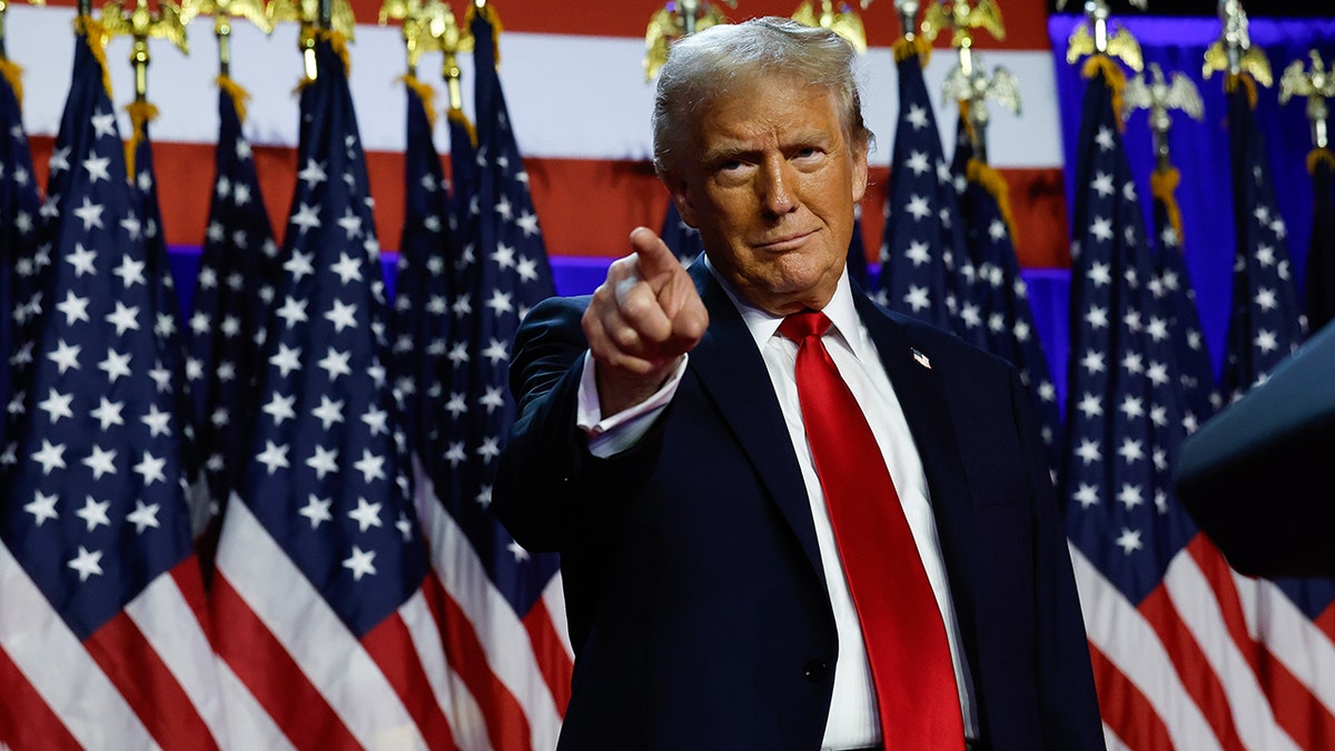 Donald Trump pointing, US flags behind him