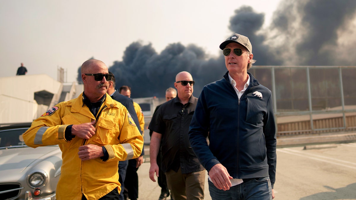 California Governor Gavin Newsom (right) tours the downtown business district of Pacific Palisades as the Palisades Fire continues to burn on January 8, 2025, in Los Angeles, California. 