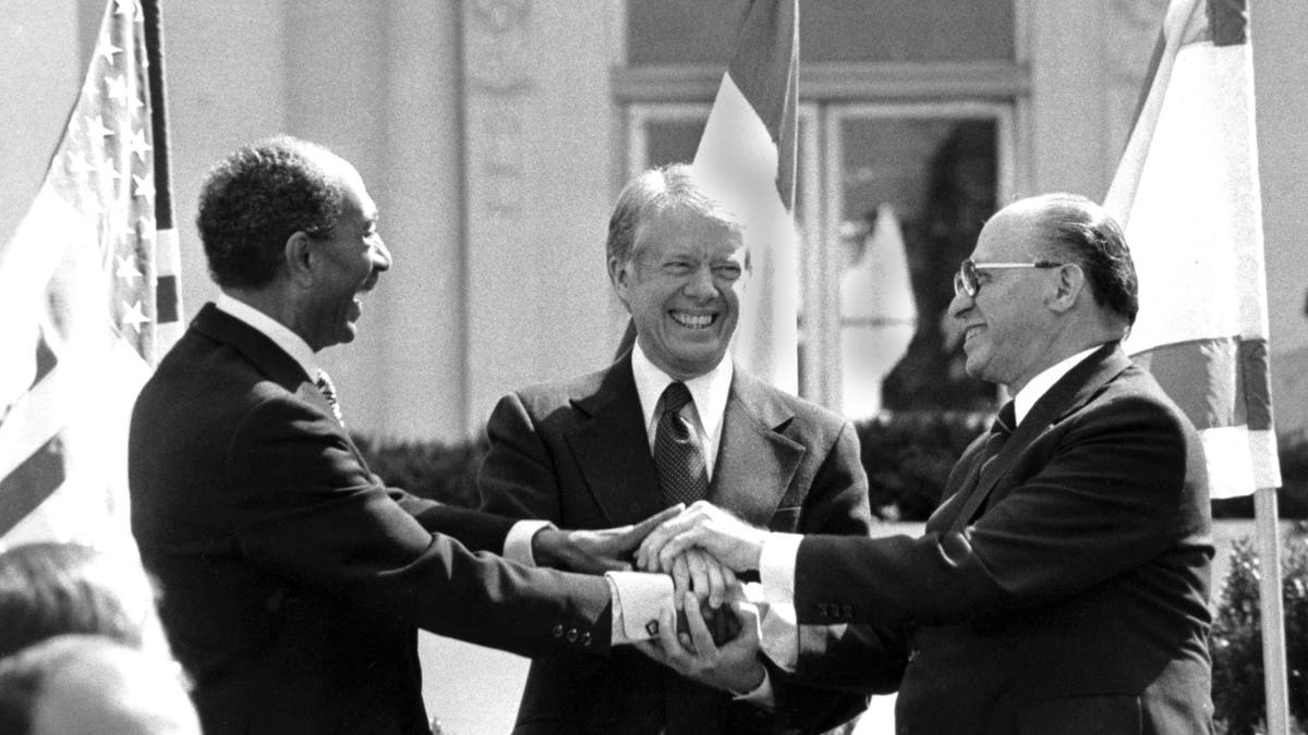 Egyptian President Anwar Sadat, left, Carter, center, and Israeli Prime Minister Menachem Begin clasp hands at the White House after signing the peace treaty between Egypt and Israel, March 26, 1979.