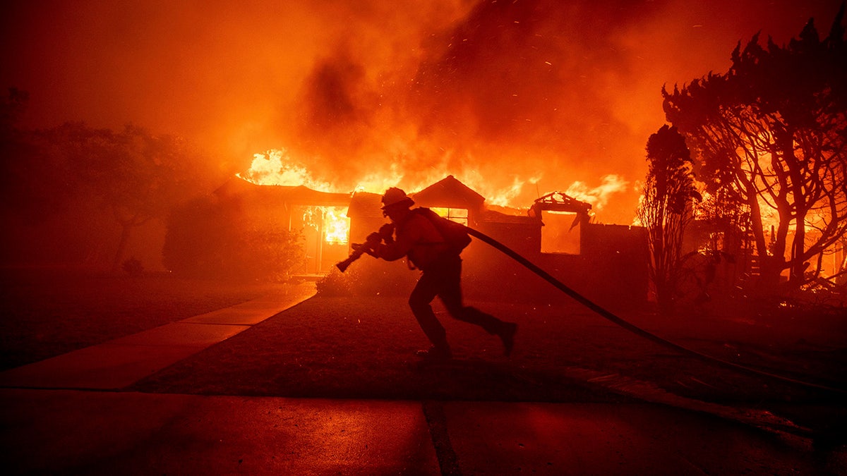 firefighter with hose as house behind him ablaze