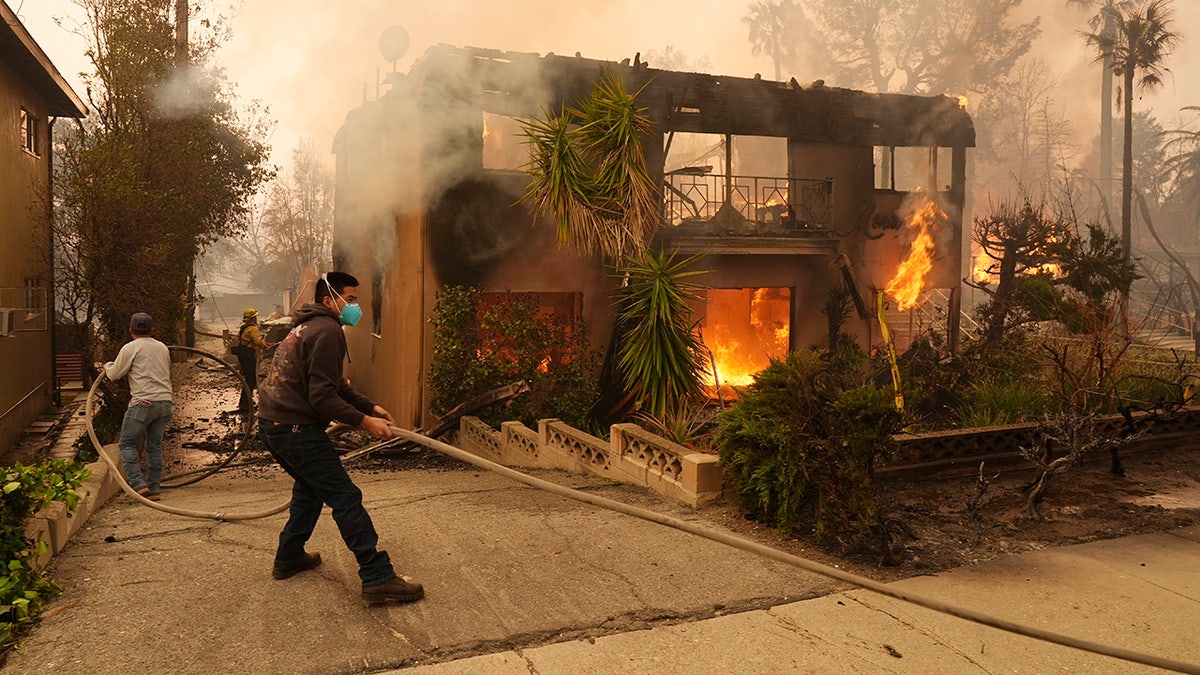 Pedestrians help a firefighter stretch a hose as an apartment building burns