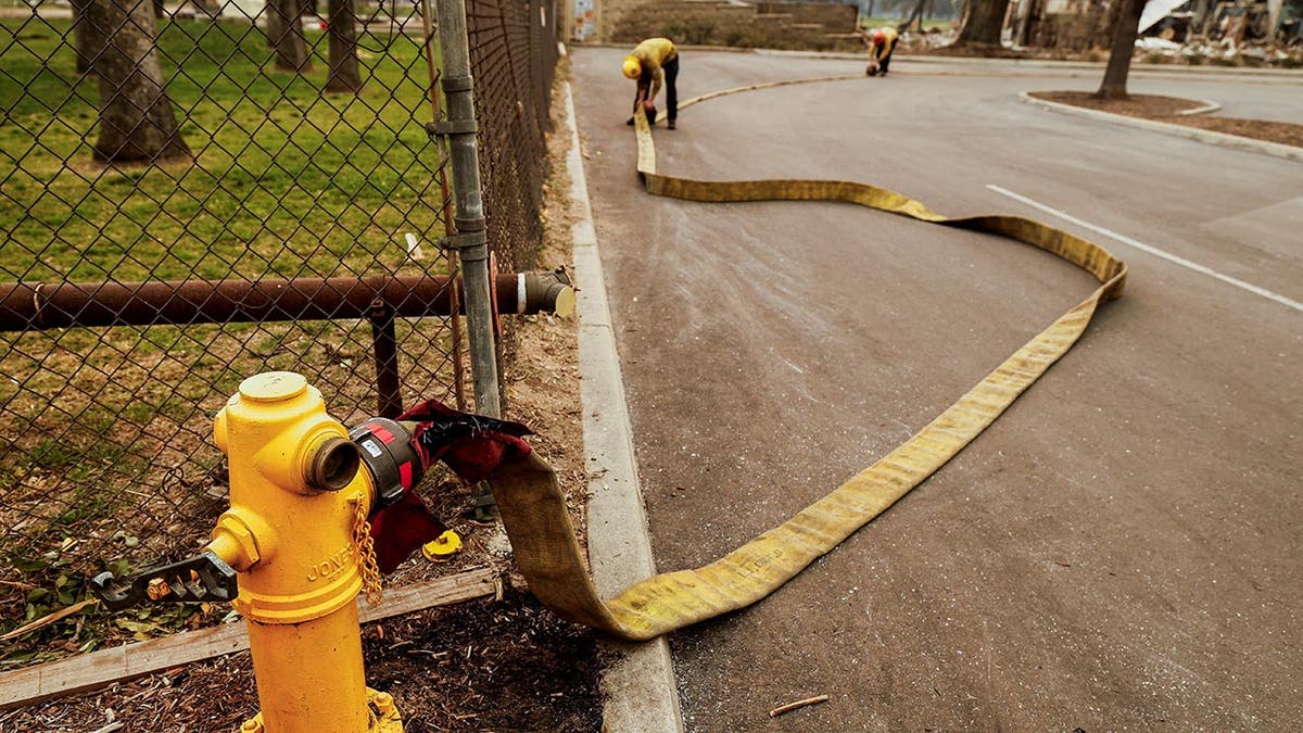 Firefighters roll up a hose used to fight the Eaton Fire