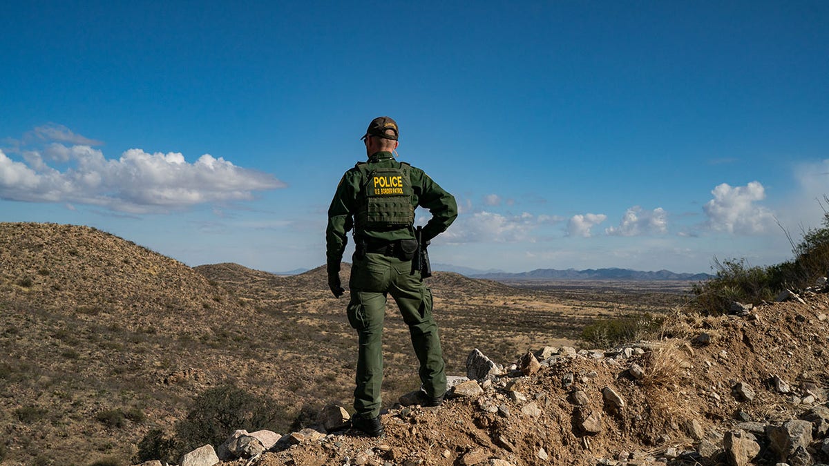 border agent on cliff searching for migrants in border area