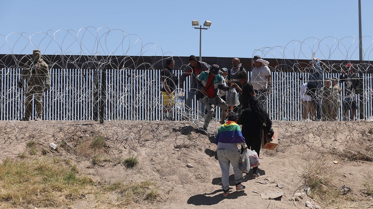 migrants in front of razor wire, wall