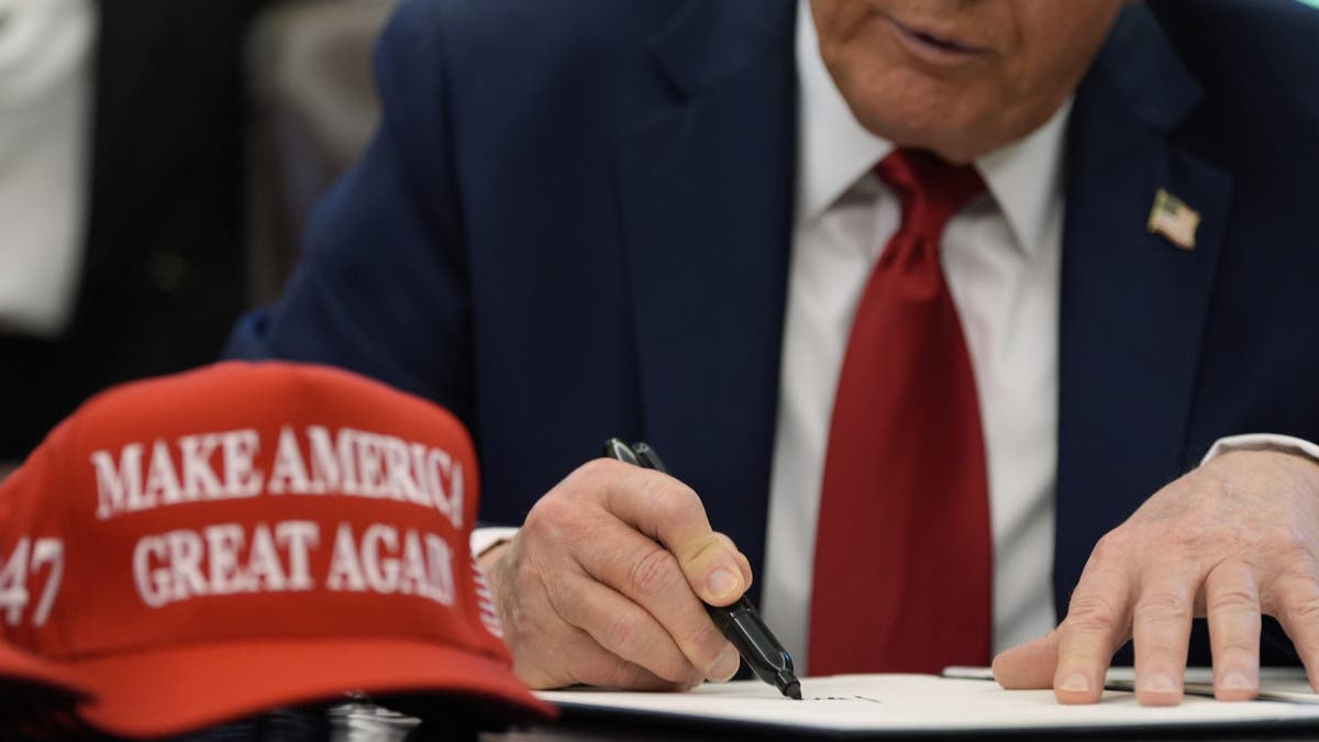 Trump signing EO with red MAGA hat on desk