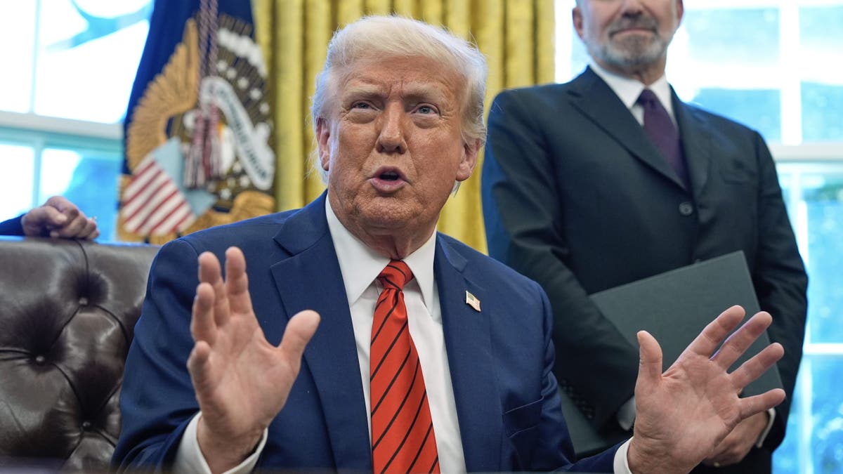 Trump at Resolute Desk, hands gesturing upward