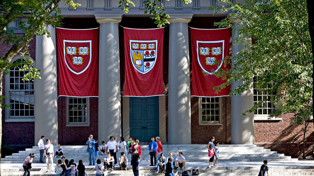 Students gather outside Harvard University's Memorial Church, with red banners displaying the Harvard crest hanging between columns at the entrance.