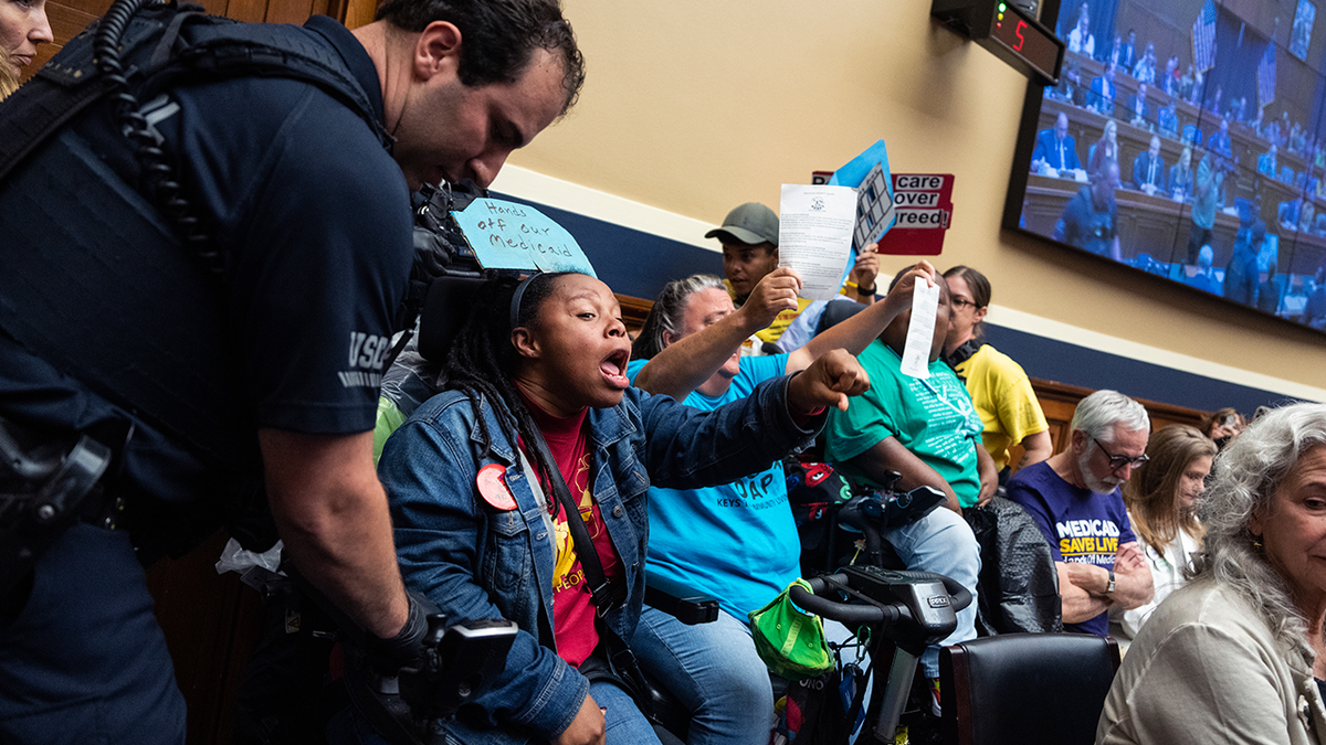 woman protesting in committee room as police start to usher her out