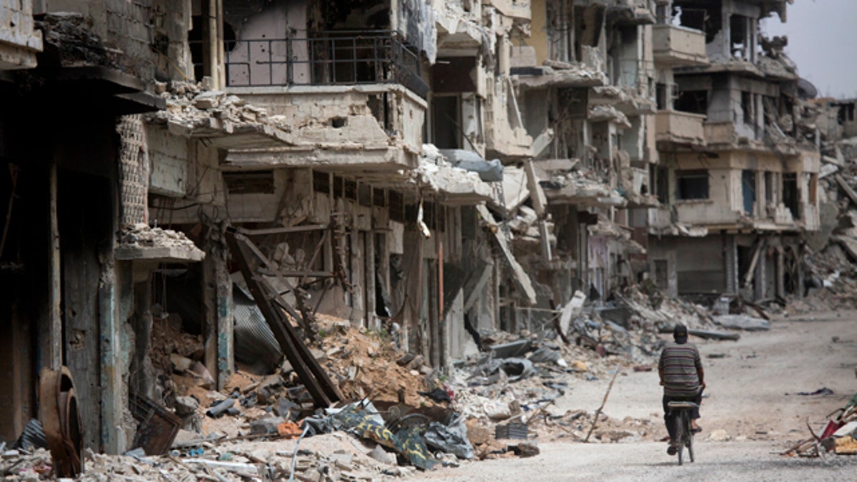 FILE - In this June 5, 2014, file photo, a man rides a bicycle through a devastated part of Homs, Syria. (AP Photo/Dusan Vranic, File)