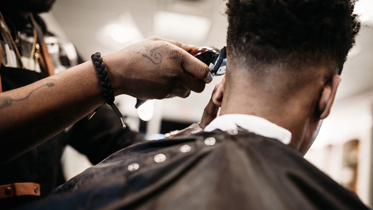 An African American man gets his hair cut by a skilled stylist at a small business barbershop.