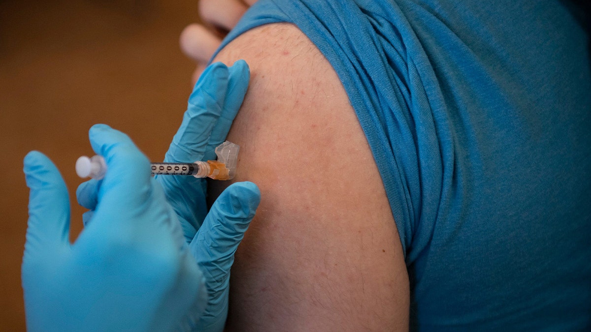 hand with gloves on administers vaccine shot to arm