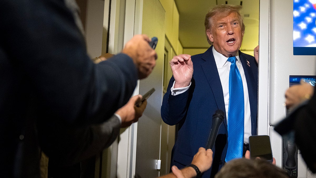 Donald Trump in blue tie speaking to reporters aboard Air Force One