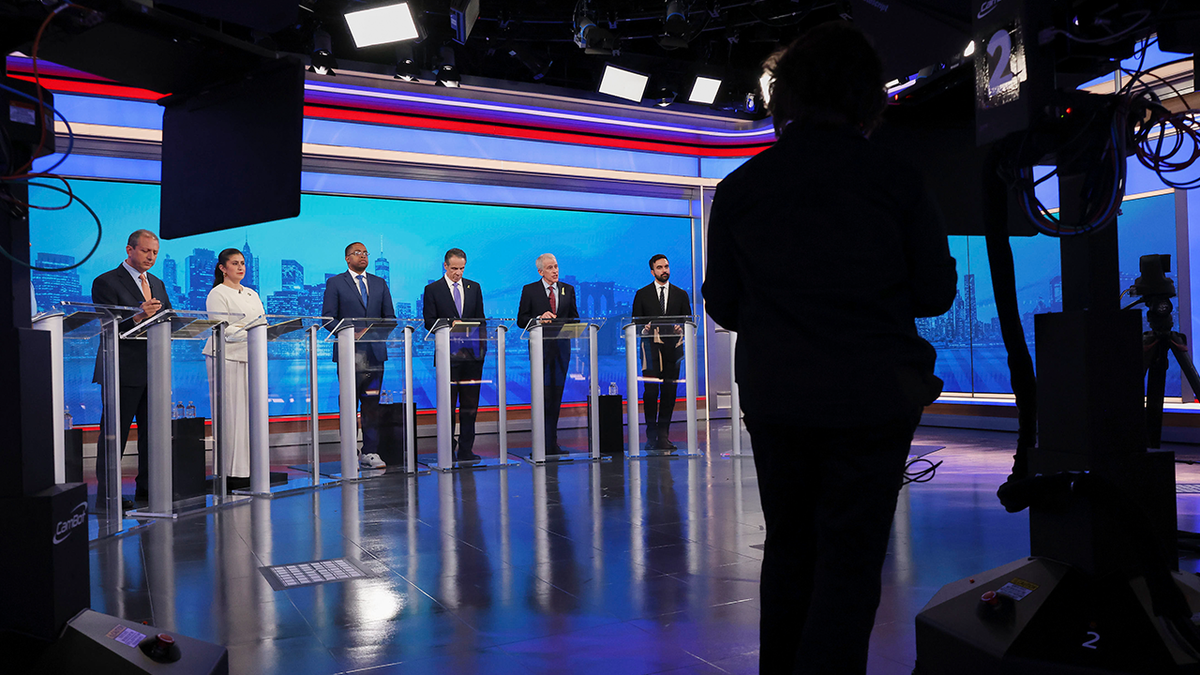 Mamdani with others in wide shot of debate stage