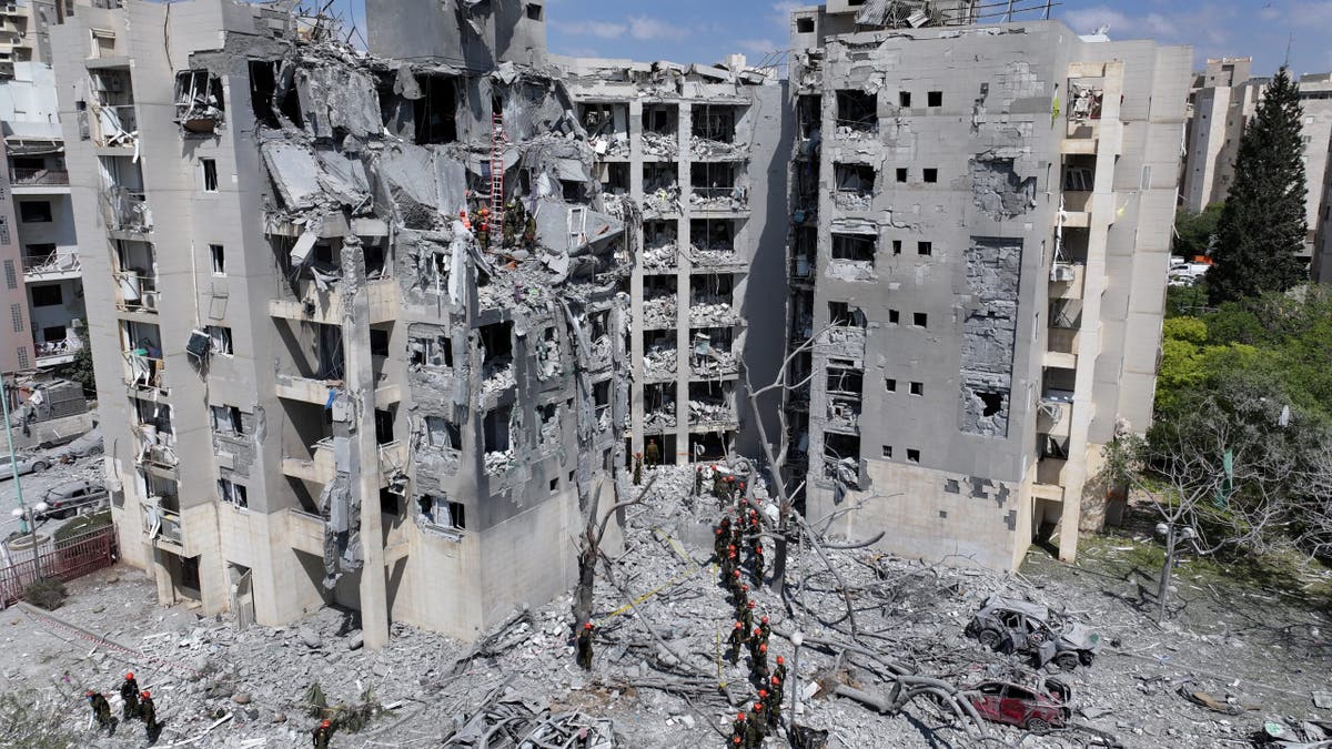 Israeli rescue workers search rubble and twisted debris outside a collapsed residential building hit in a recent airstrike.