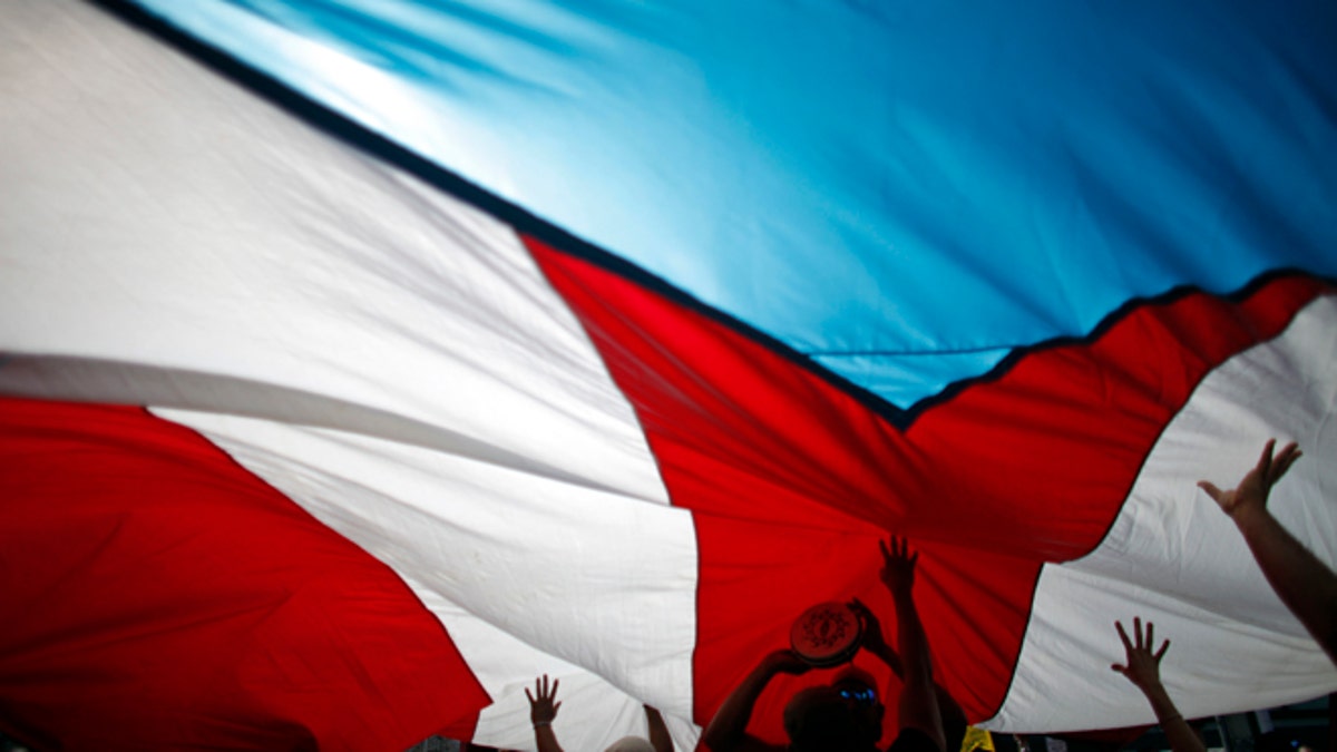 FILE - In this Jan. 15, 2014 file photo, demonstrators touch a giant Puerto Rican flag from underneath as they protest at the labor department during a teachers strike in San Juan, Puerto Rico. From the intriguing to the impossible, there is no shortage of ideas for fixing Puerto Ricos ailing economy as the government tries to dig out from a whopping $70 billion in public debt and bring back economic growth. (AP Photo/Ricardo Arduengo, File)