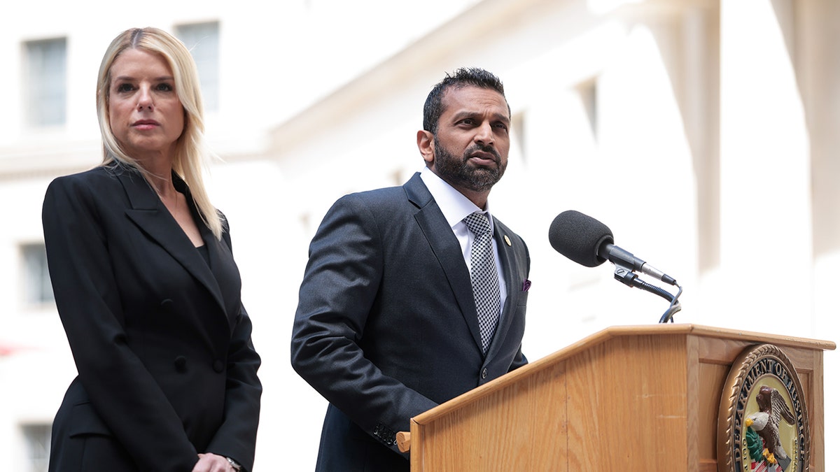 Bondi listens as Patel speaks at a podium 