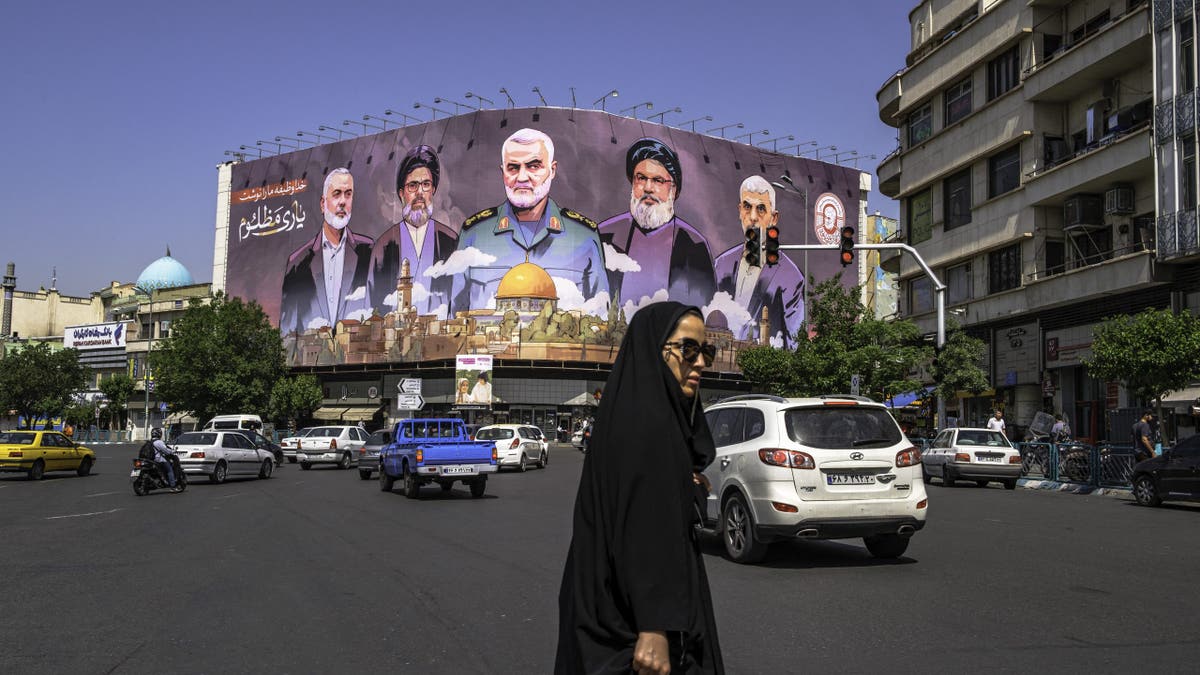 giant mural in Iran in background, woman in black in foreground