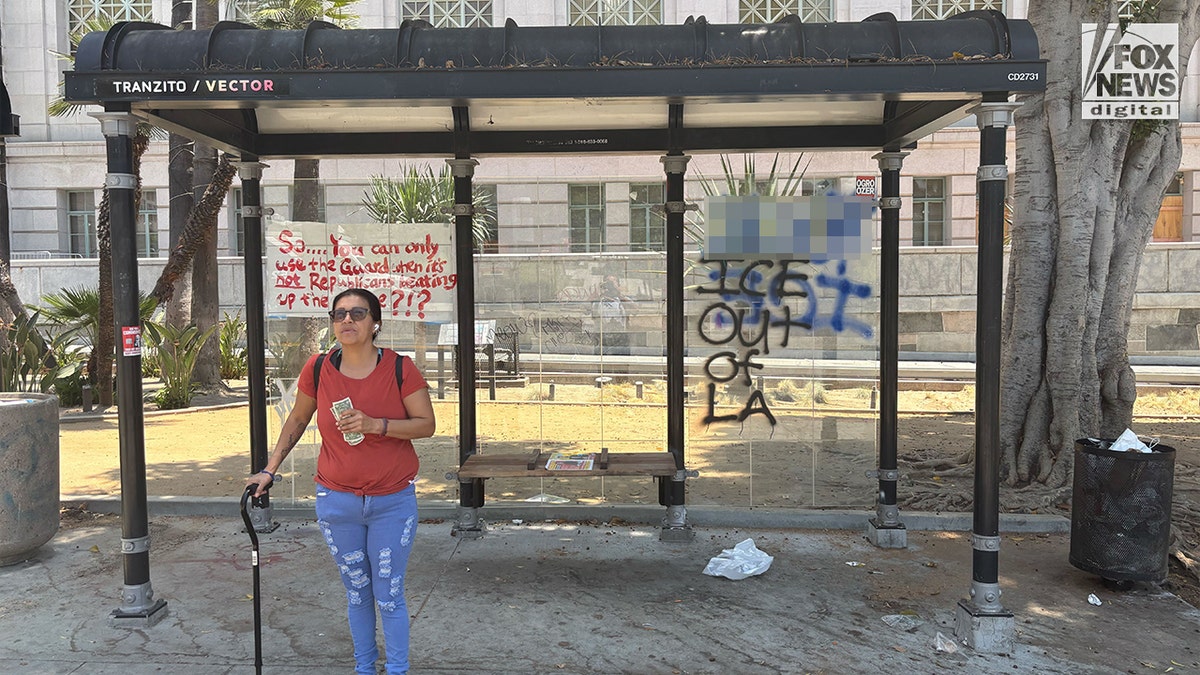 Woman stands in front of graffitied bus stop in downtown Los Angeles