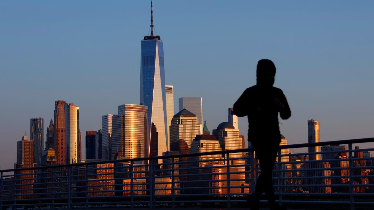 The sun sets on the skyline of lower Manhattan and One World Trade Center in New York City as a person runs along the Hudson River on February 25, 2024, in Jersey City, New Jersey.