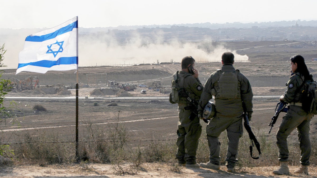 Israeli soldiers on ridge looking down hill to settlement