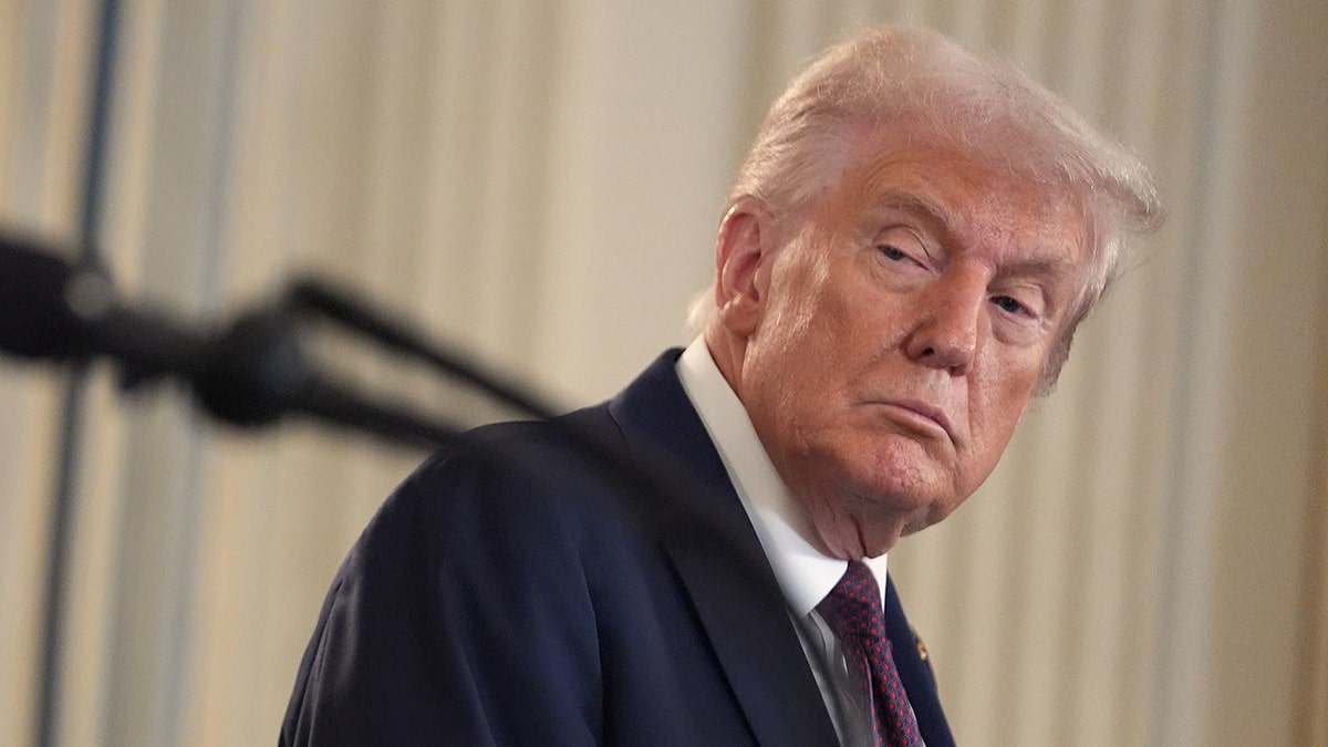 Donald Trump wearing a dark suit turns his head to listen during a news conference