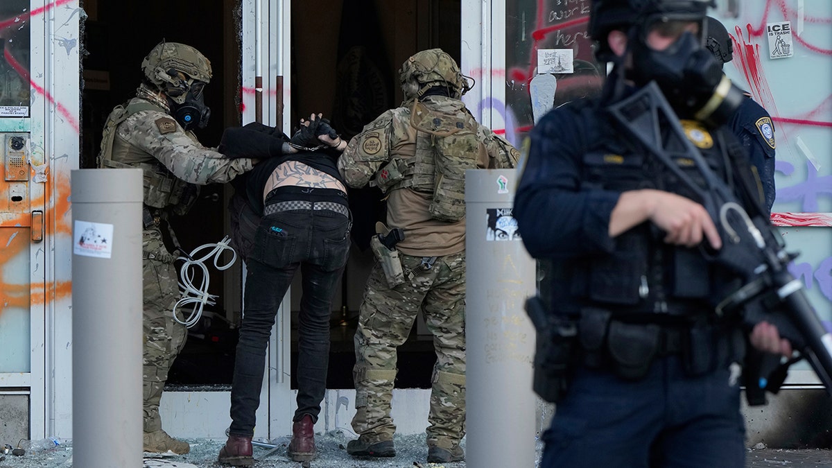 Border Protection agents detaining person outside ICE building that is covered in graffiti