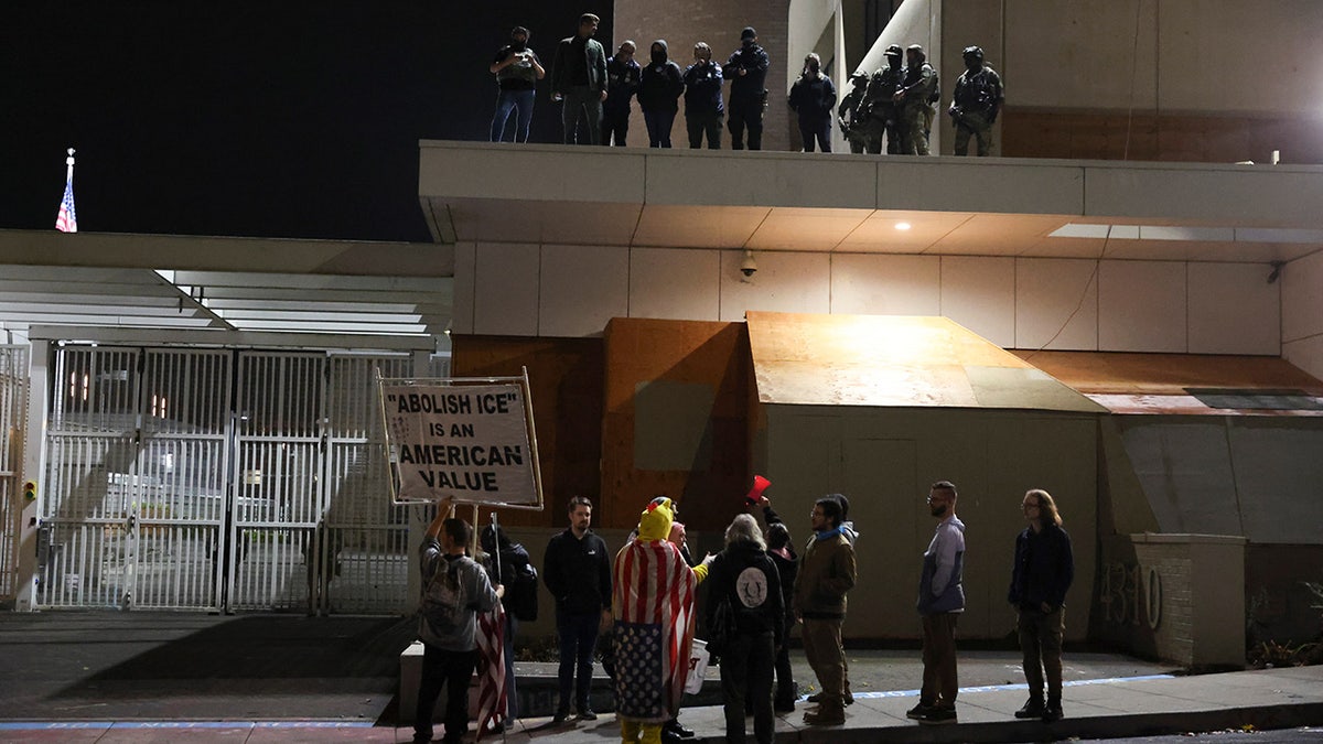 People protest outside a U.S. Immigration and Customs Enforcement facility as federal agents watch from the rooftop, in Portland, Oregon, Wednesday, Oct. 1, 2025. (AP Photo/Amanda Loman)