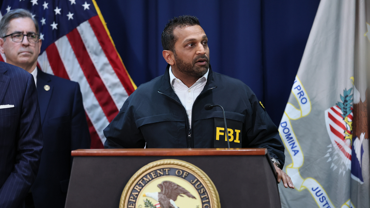 An image of Kash Patel speaking at a podium during a press conference