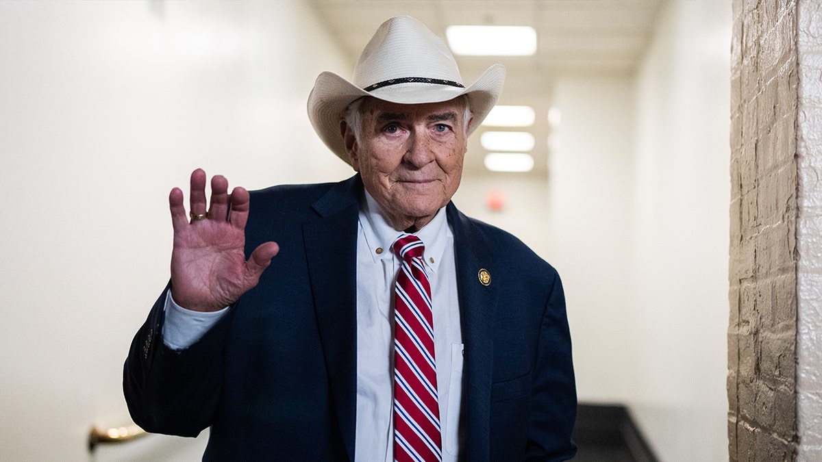 John Carter wearing white cowboy hat and suit waving.