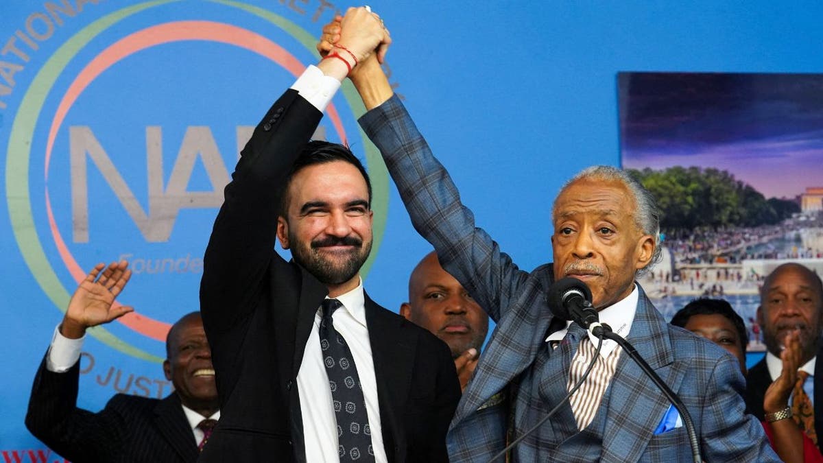 Zohran Mamdani and Al Sharpton raise joined hands on stage at the National Action Network’s House of Justice in Harlem.