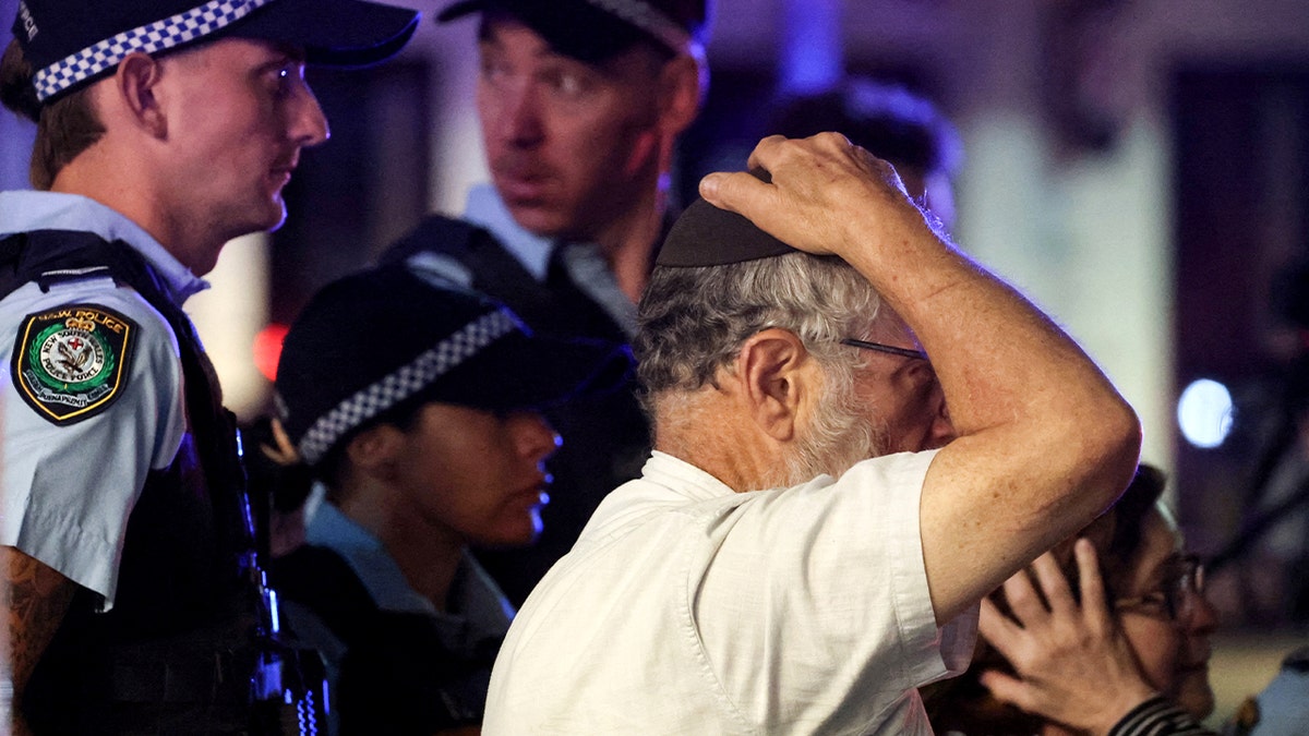 A man escorted by police shows visible distress while approaching an active investigation area.