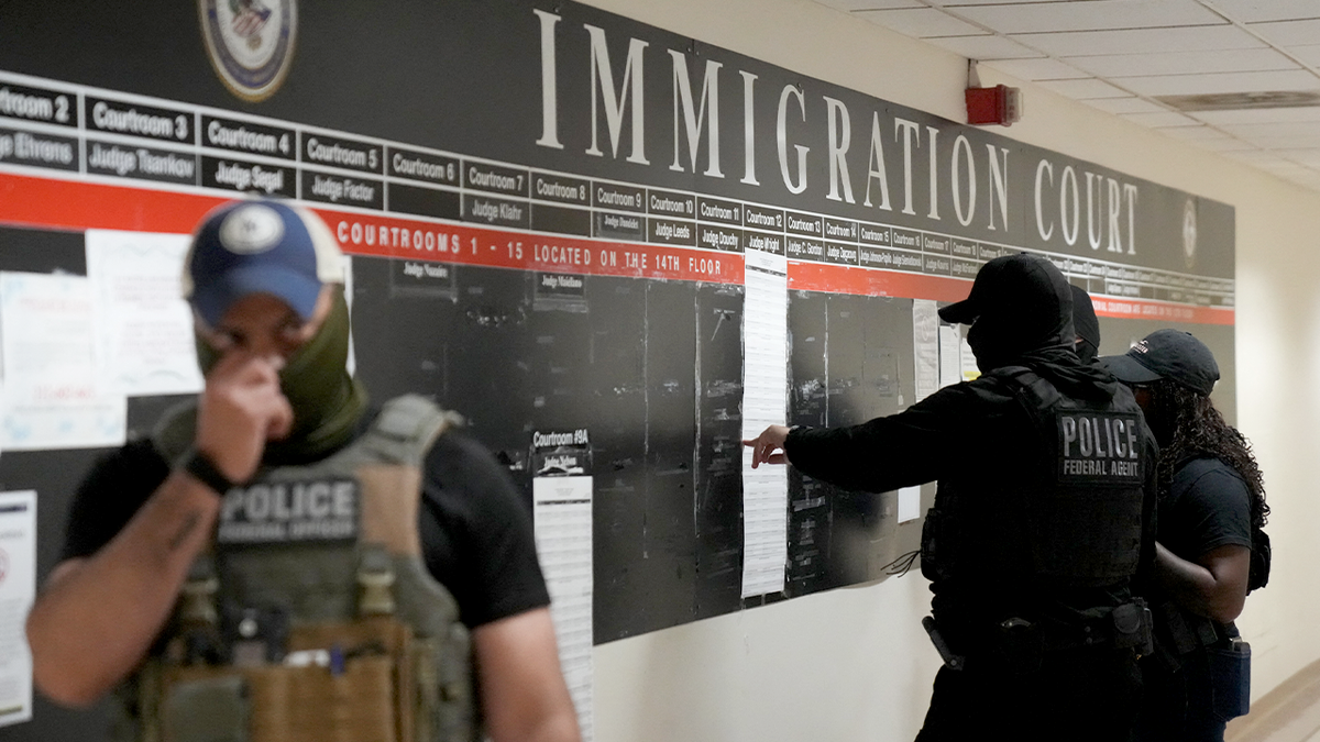Plainclothes immigration agents review paperwork inside a courthouse hallway.
