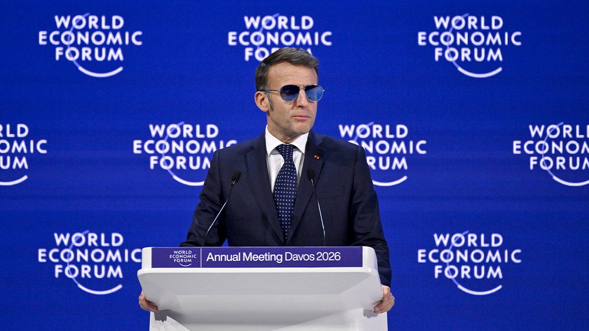 A French leader stands at a podium addressing an international audience at a global economic summit.