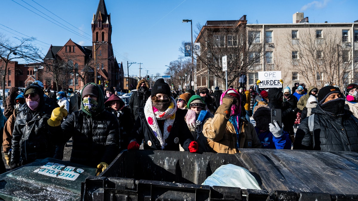 Protesters stand behind trash cans