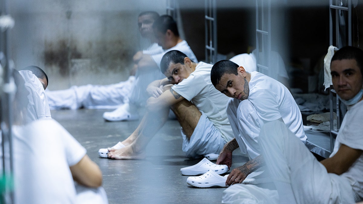 TDA members at CECOT on the ground sitting in white uniforms and crocs