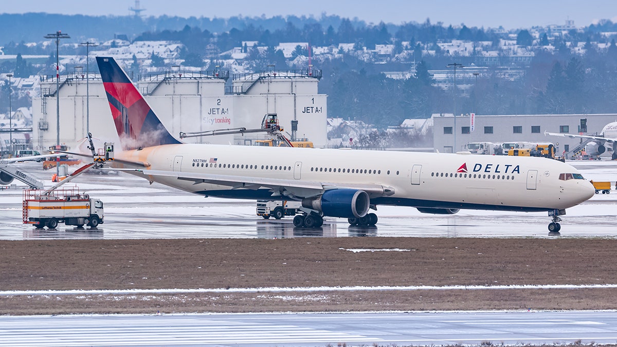 Delta Air Lines wide-body aircraft undergoing de-icing on a snowy airport tarmac during winter operations.